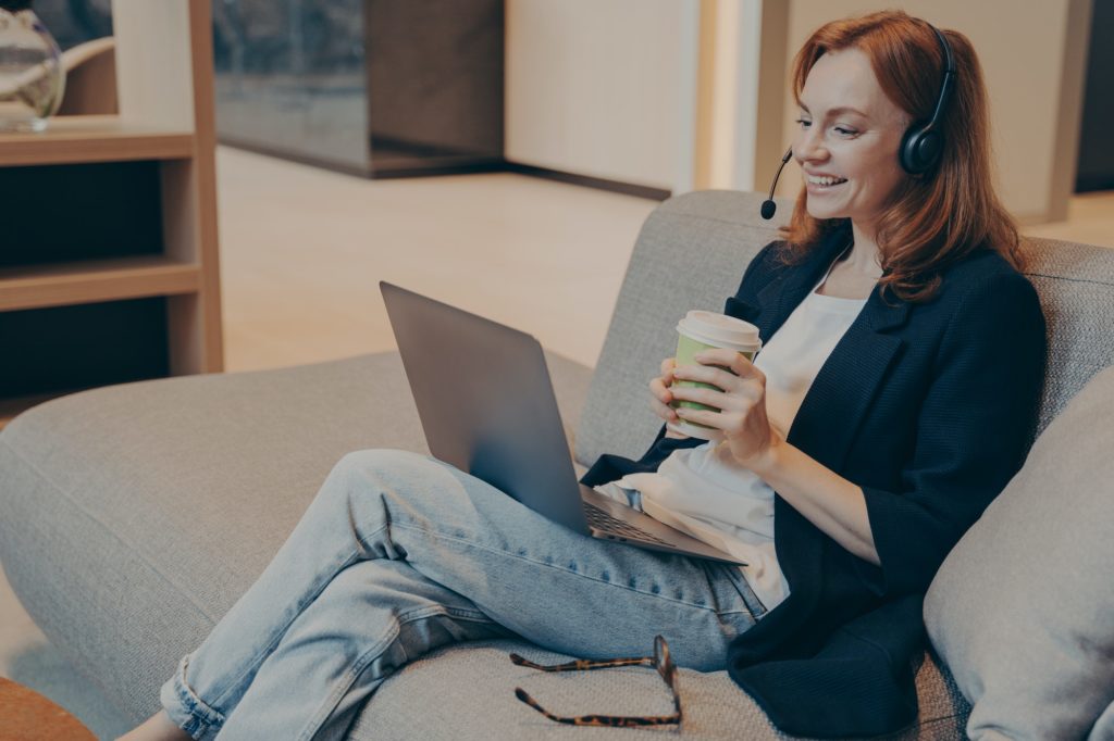 Happy millenial woman wearing headphones and smiling while watching online webinar course on laptop